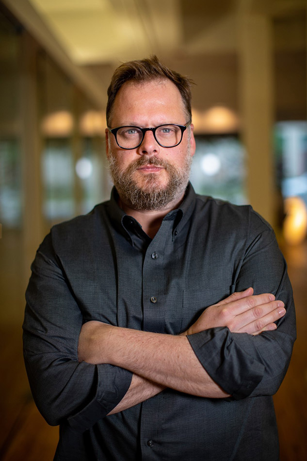 White man with beard and glasses wearing a dark button-down shirt