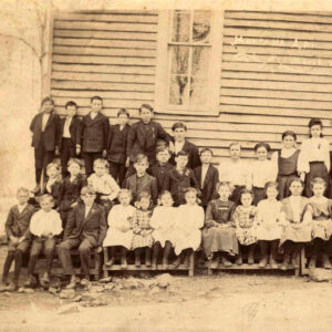 Large group of white children and adults in front of wooden building