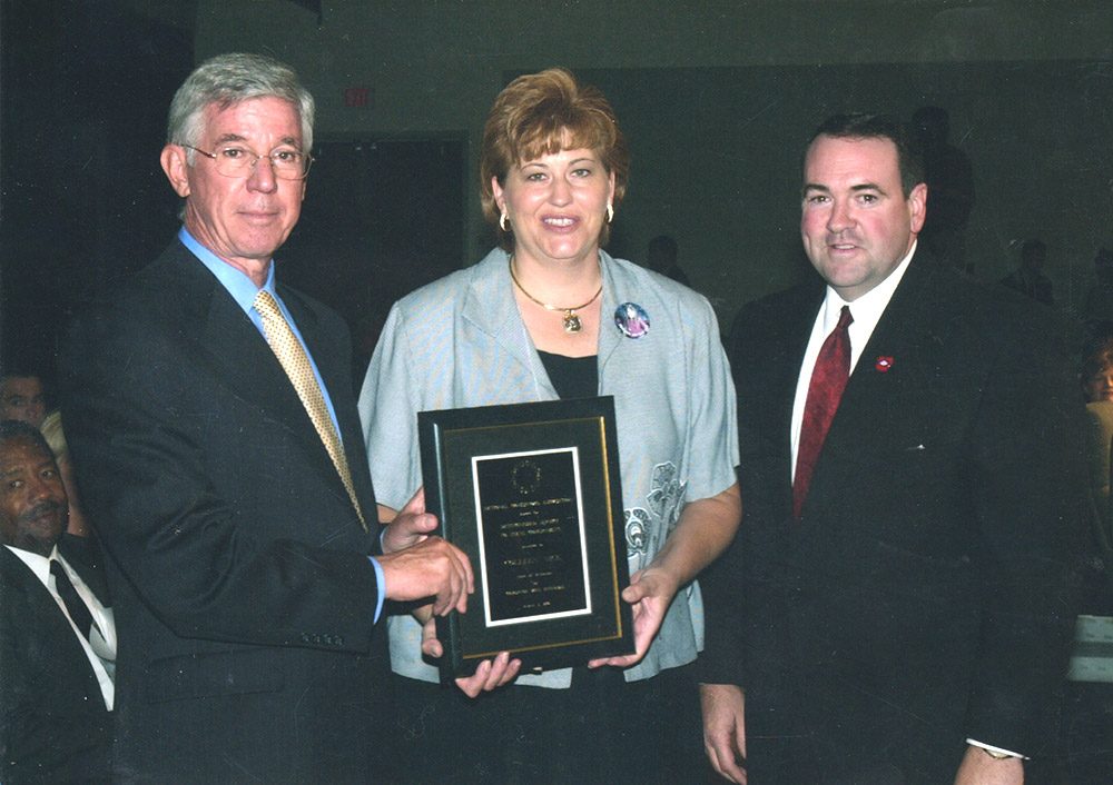 Two white men and one white woman holding award