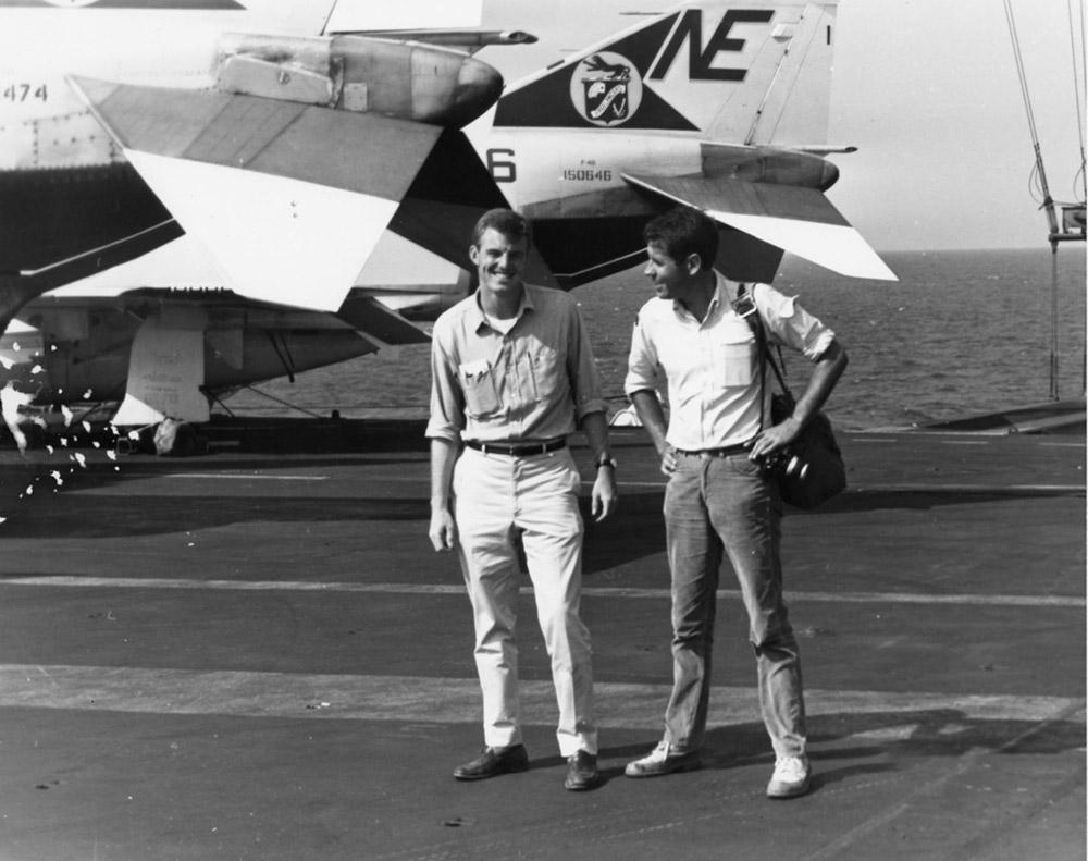 Two white men standing near a plane on board a ship