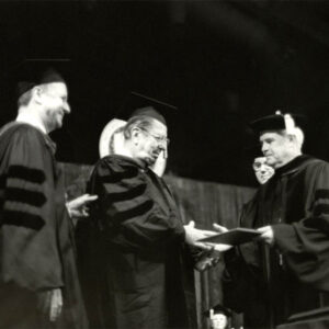 White men standing on stage wearing academic robes