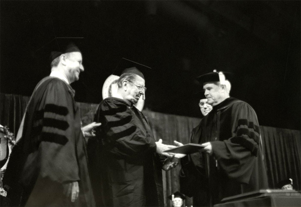 White men standing on stage wearing academic robes