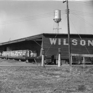 Metal building with bales of cotton and water tower in background