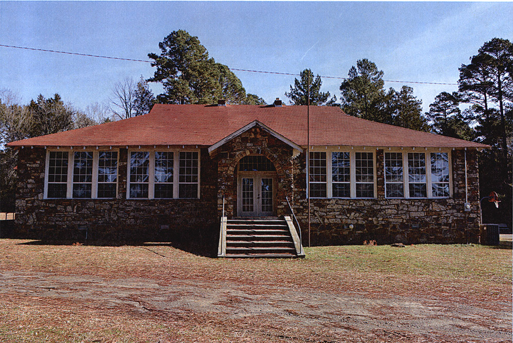 one-story rock school building with windows in front and red shingle roof