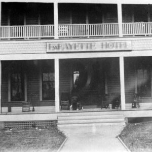 Multistory wooden building "Lafayette Hotel" with rocking chairs and people standing on lower porch