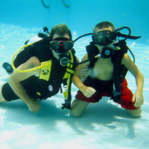 One white adult and one child under water with scuba gear