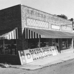 brick building with a striped awning and a sign leaning on it saying  "Baxter County Democrat Headquarters"