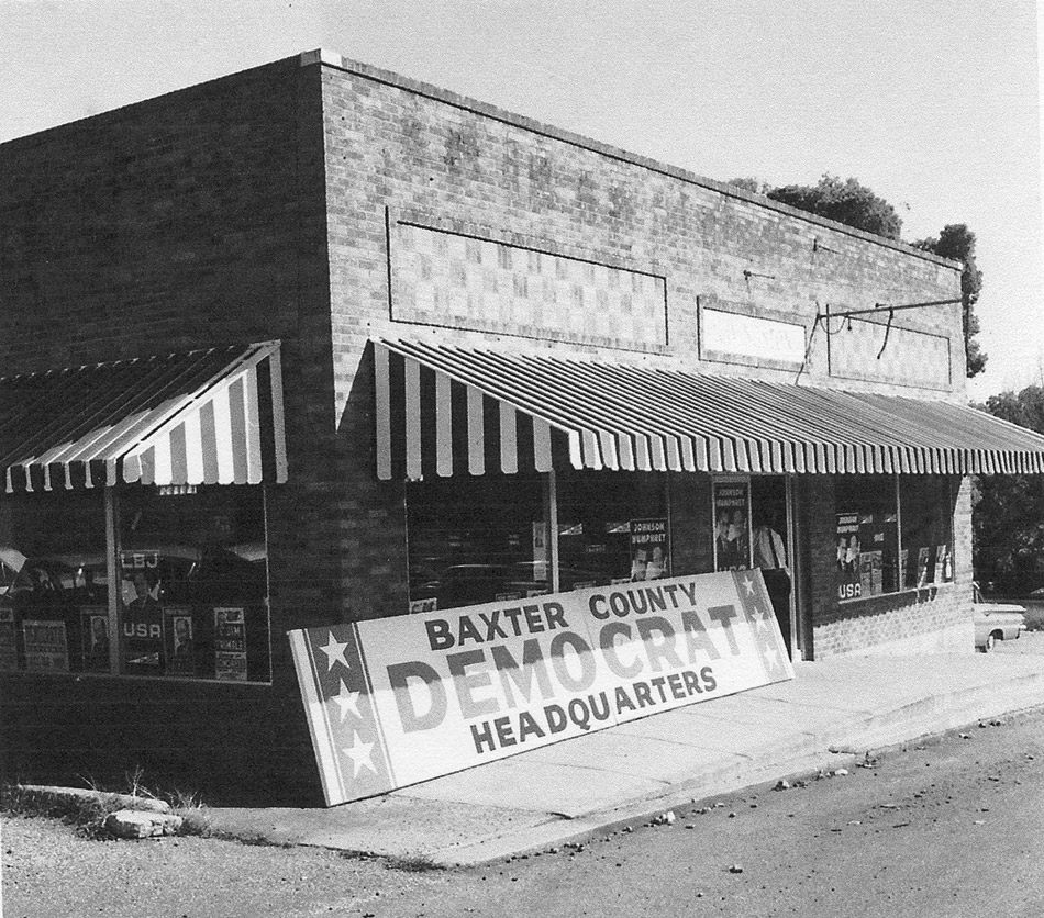 brick building with a striped awning and a sign leaning on it saying  "Baxter County Democrat Headquarters"