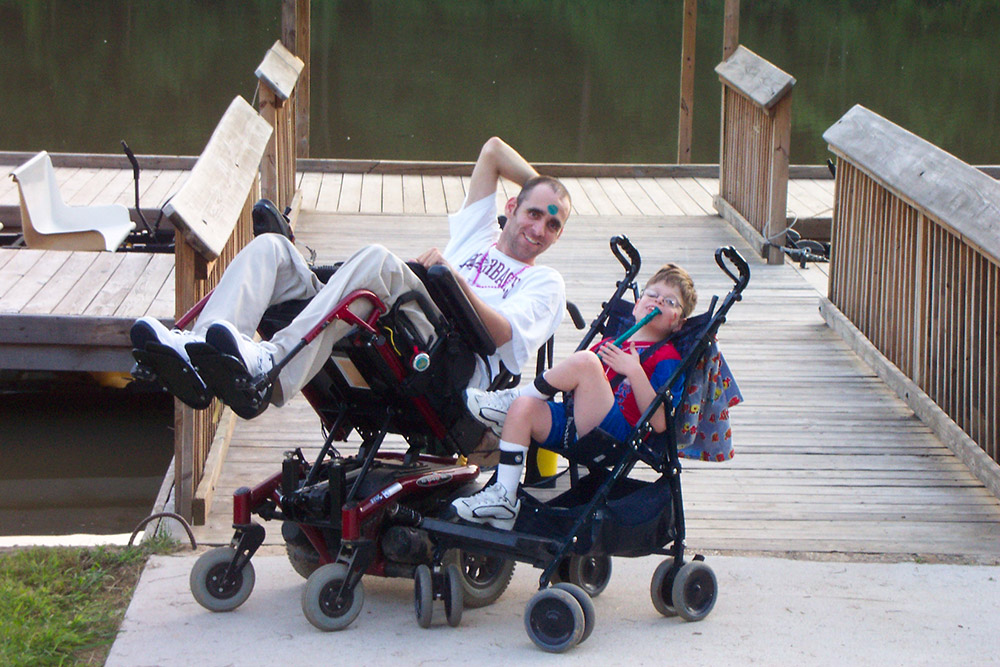Two white people in wheelchairs posing on a boat dock
