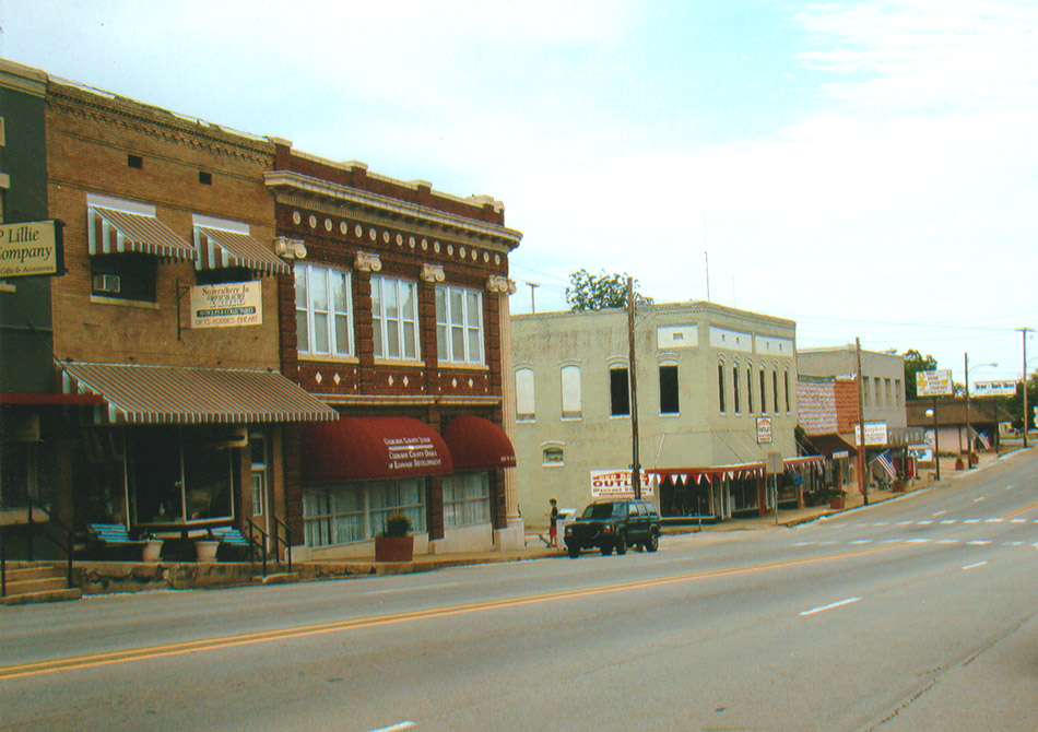 Row of two-story and one-story storefront buildings along paved road