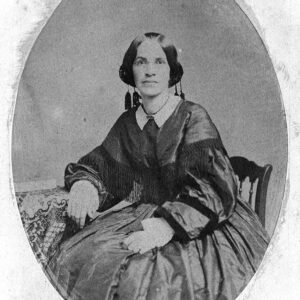 White woman in heavy-looking dress and round glasses
