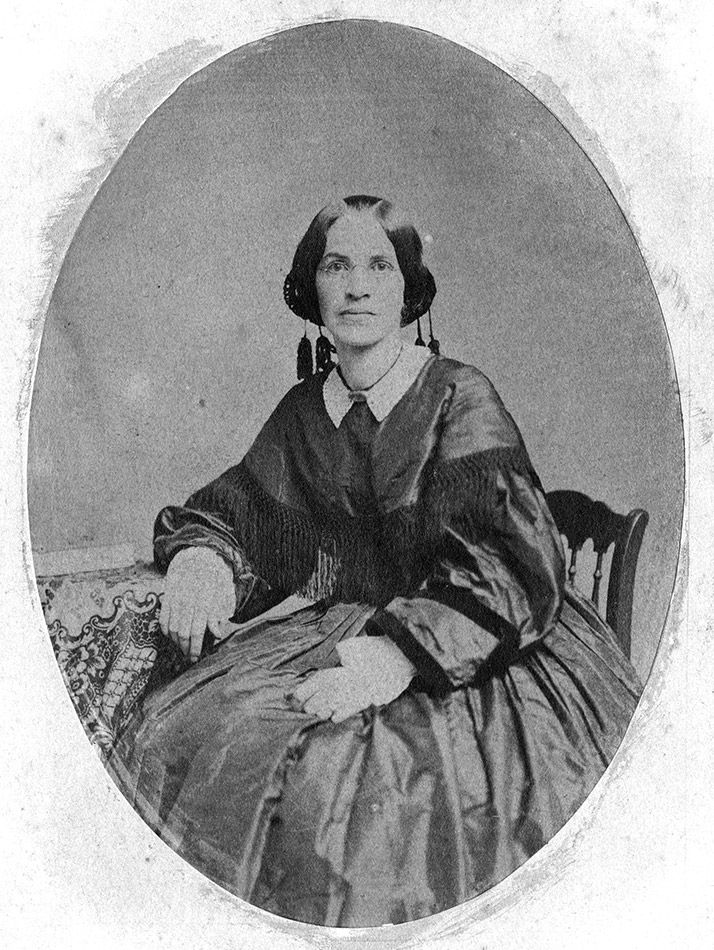 White woman in heavy-looking dress and round glasses