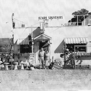 White man and woman standing before single story building with a sign on the top saying "Ozark Souvenirs"
