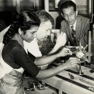 Asian man in suit and tie overseeing a male and a female student as they operate a piece of laboratory equipment