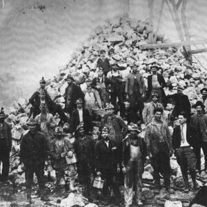 Group of white men in helmets standing before huge pile of rocks