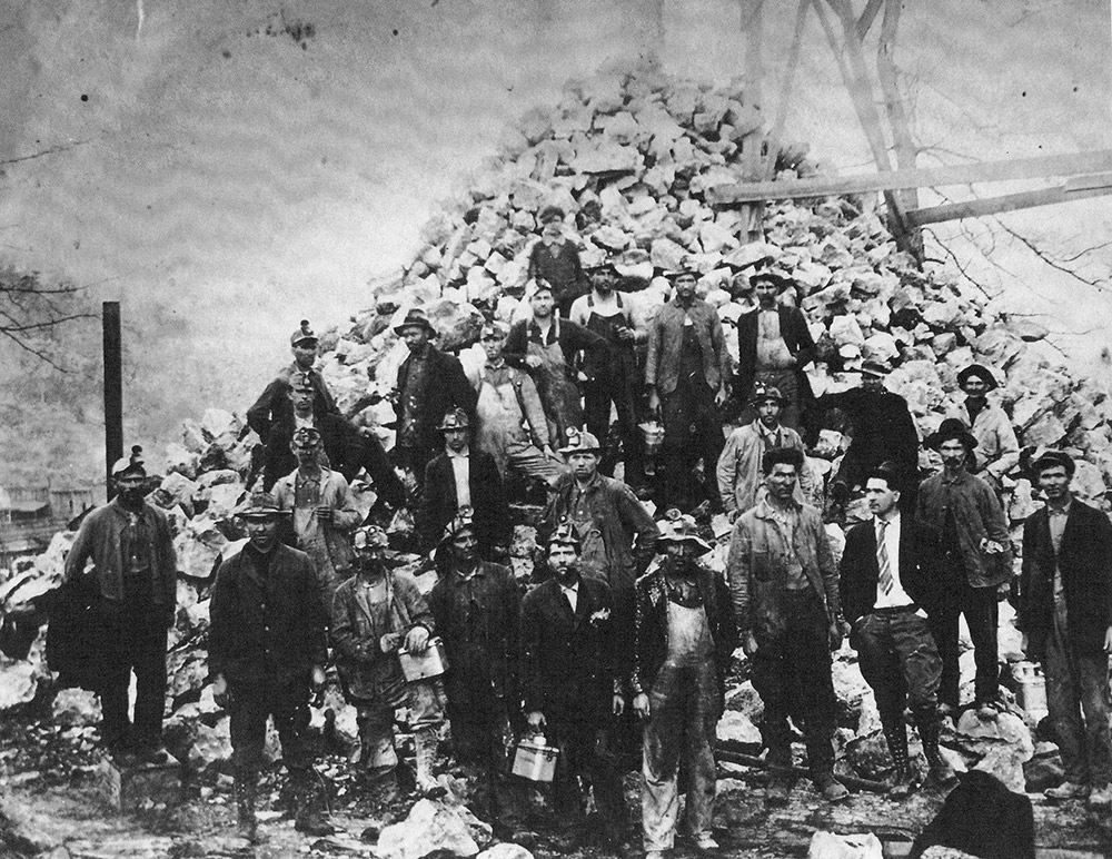 Group of white men in helmets standing before huge pile of rocks