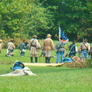 White men dressed up as soldiers in field with trees in background
