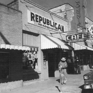 Men standing on sidewalk in front of a multistory brick building with a sign on the top saying "Republican Headquarters"