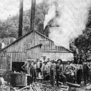 Group of white men standing in work hats before building that is belching smoke
