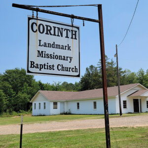 Single story white concrete block church building with sign saying "Corinth Landmark Missionary Baptist Church"