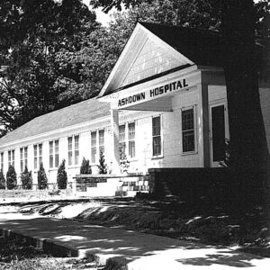 Single story white wooden building with "Ashdown Hospital" in lettering above the porch
