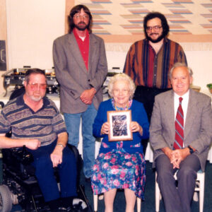 Group of white men gathered around older white woman holding framed certificate