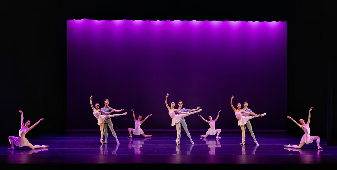 Men and women doing ballet on a stage with purple lights