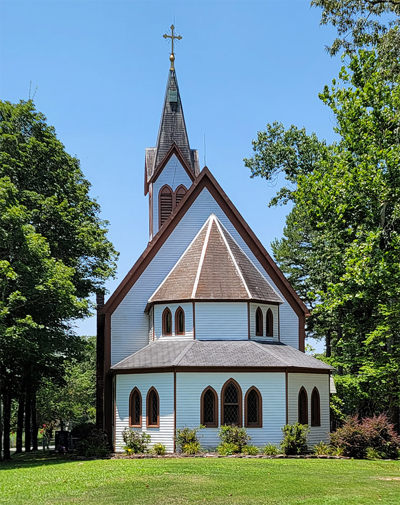 Multistory wooden white church building with brown roof and steeple with cross on top