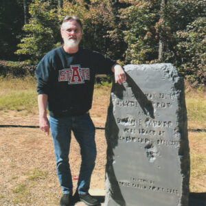 Man with beard standing next to engraved stone