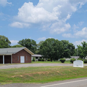 Single story red brick church building with three white crosses in the ground