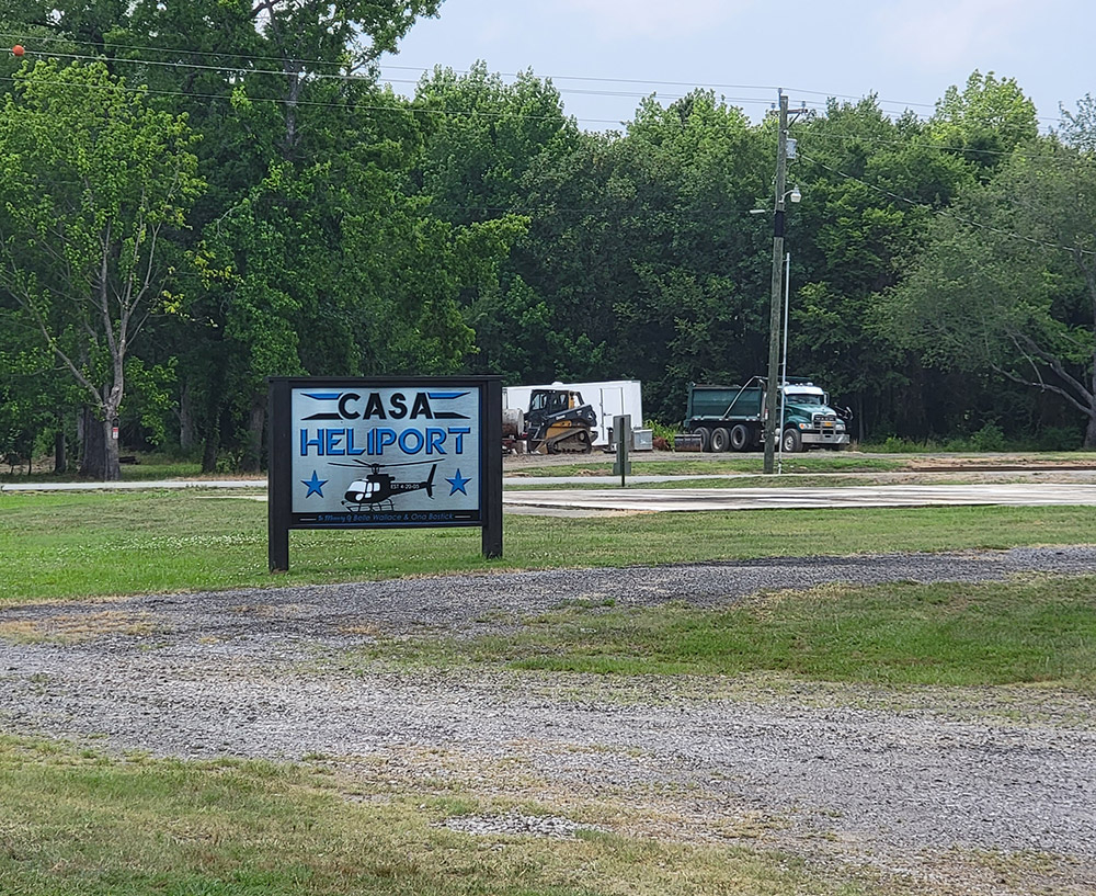 Grass and rock landing area with sign picturing helicopter saying "Casa Heliport"