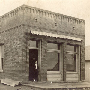 White man in suit and tie standing in doorway of brick building with tall windows