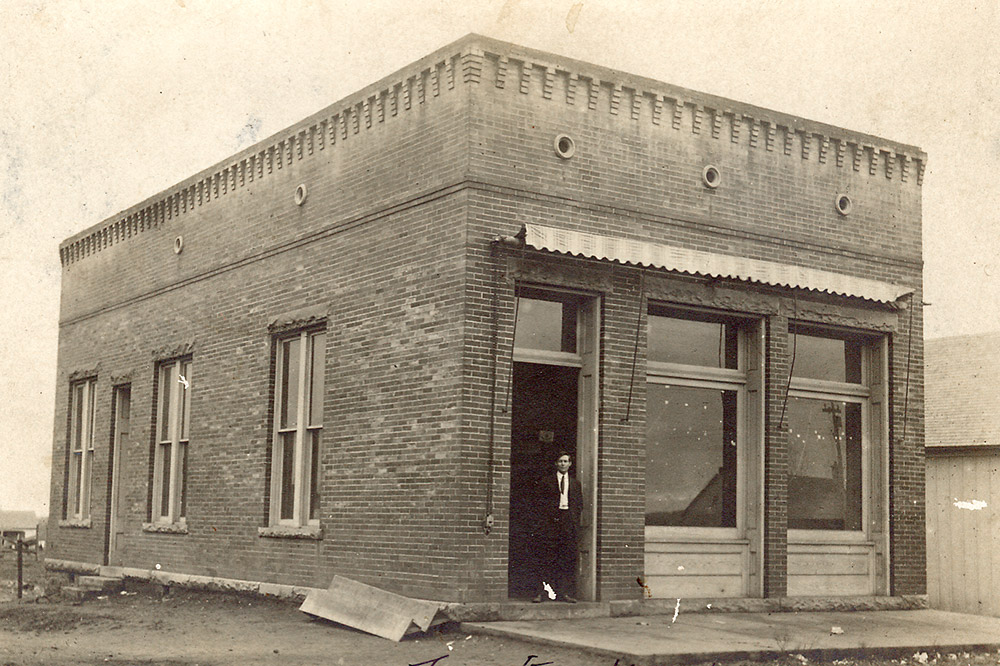 White man in suit and tie standing in doorway of brick building with tall windows