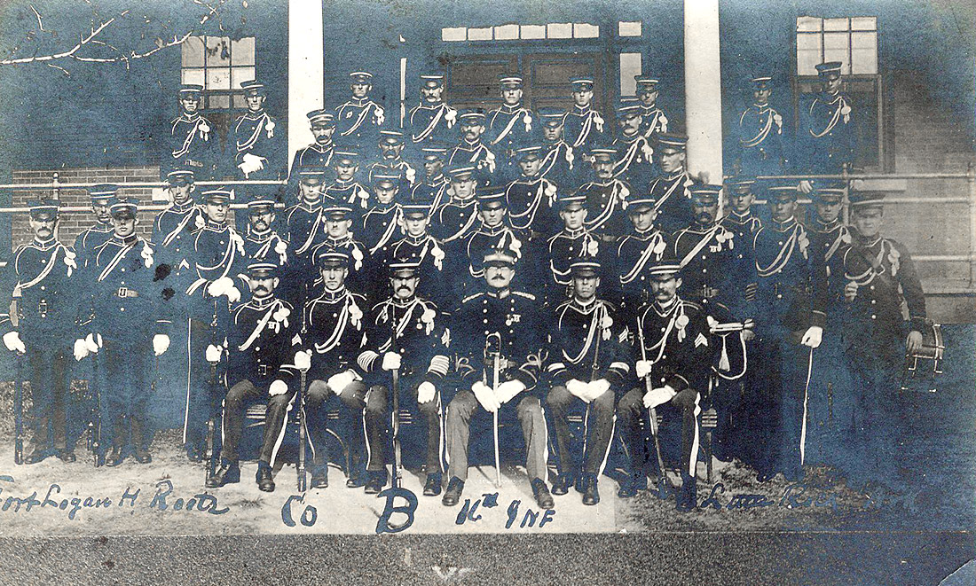 Large group of white men posing for group photo wearing military garb and holding rifles