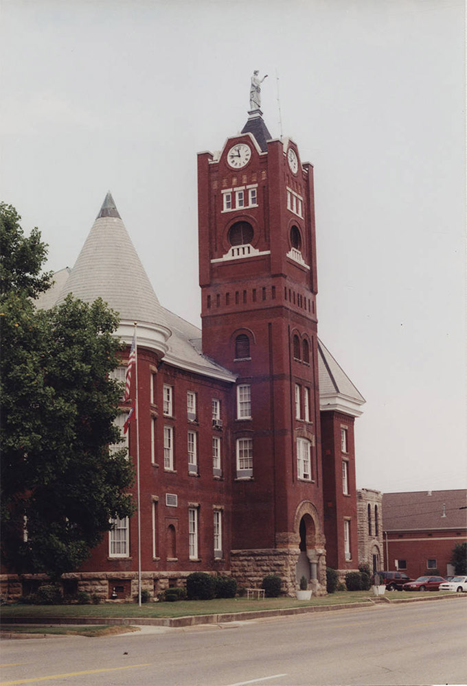 Multistory red brick building with large clock tower with statue atop it and a round tower next to it