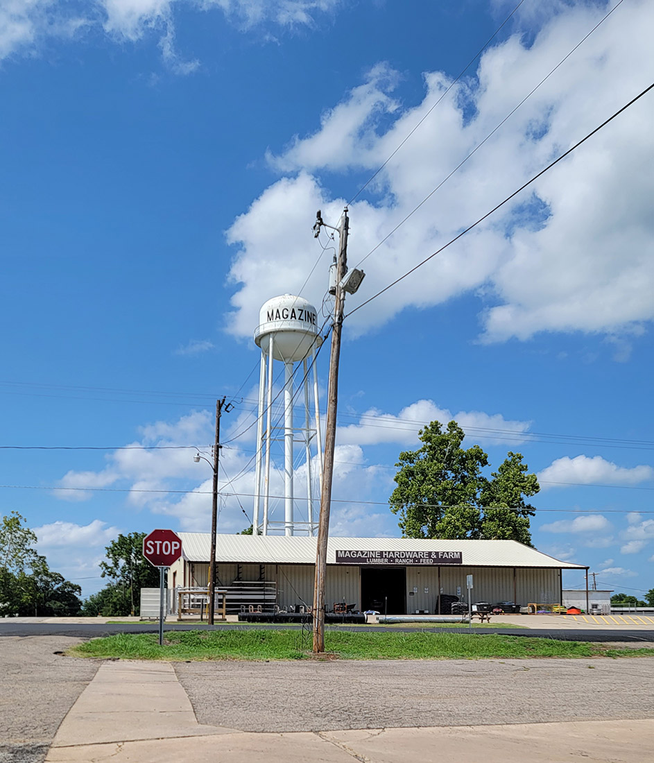 intersection and a hardware store with a water tower in the background with the word "Magazine" on it