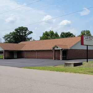 Single story tan brick church building with large parking lot