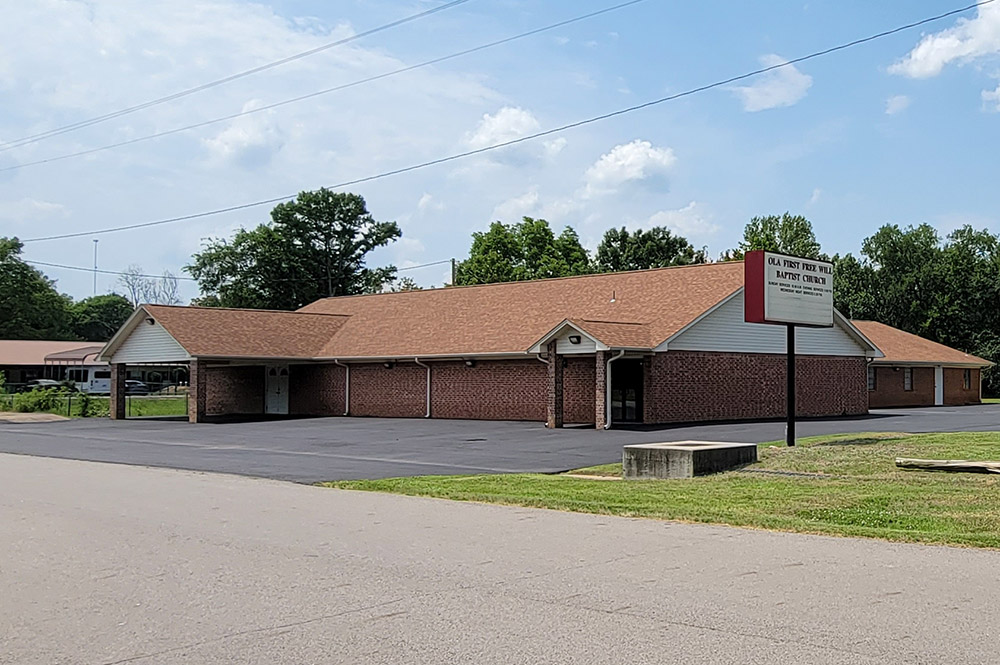 Single story tan brick church building with large parking lot