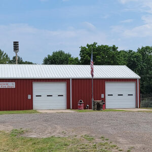 Single story red metal building with white roof and two white bay doors