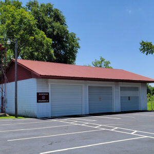 Single story white concrete block building with three bay doors and parking lot