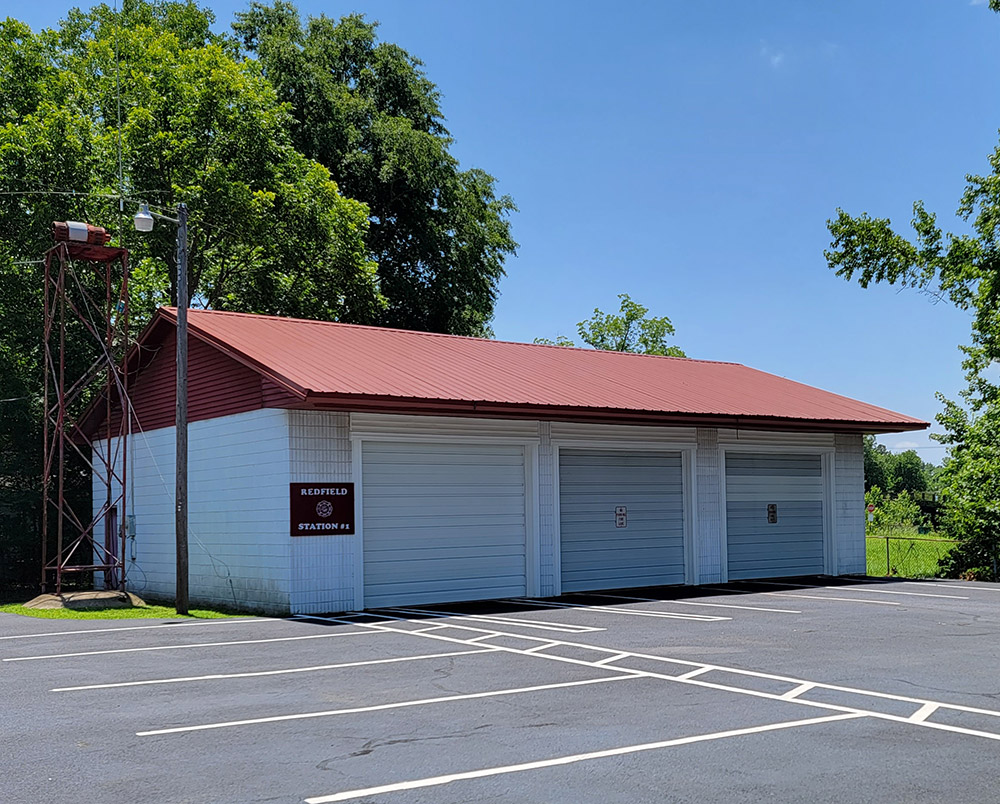Single story white concrete block building with three bay doors and parking lot