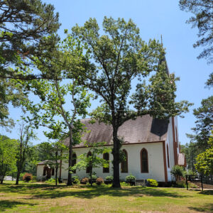 Multistory wooden white church building with brown roof and steeple amid trees
