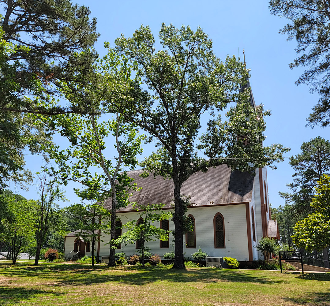 Multistory wooden white church building with brown roof and steeple amid trees
