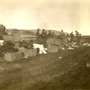 Group of soldiers in military garb standing on flat landscape by boxes and piles of equipment