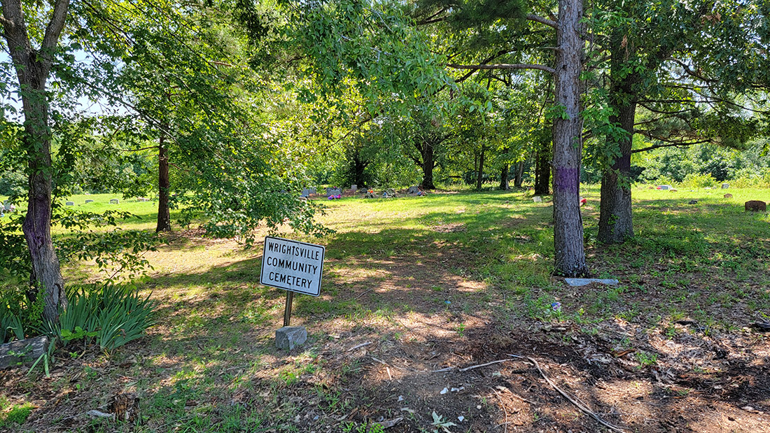 Gravestones among trees with sign saying "Wrightsville Community Cemetery"
