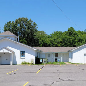 Single story white concrete block church building with parking lot