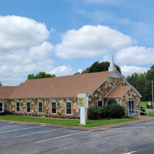 Rock church building with steeple and parking lot