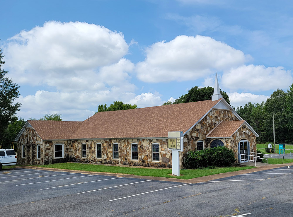 Rock church building with steeple and parking lot