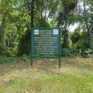 Game and Fish Commission sign listing rules about Barnett Lake with trees in background