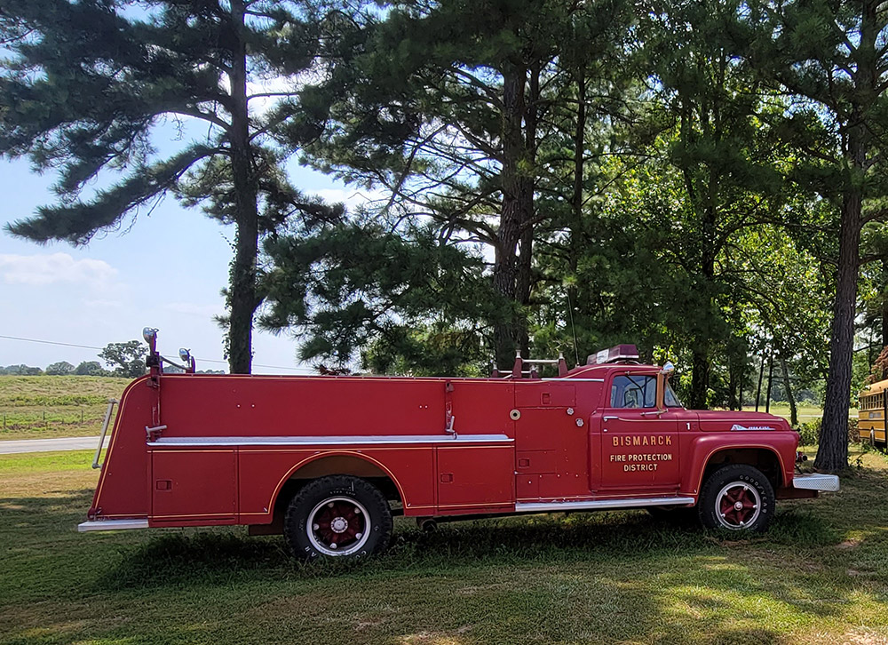 Antique red fire engine parked on grass with trees in background